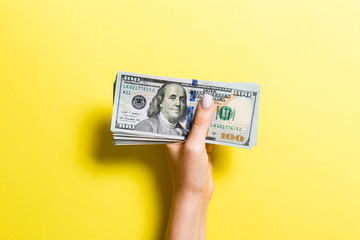 Top view of female hand giving one hundred dollar bills on colorful background. Charity and donation concept