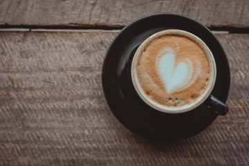 Top view, Hot coffee, heart shape with milk latte on top of black ceramic cup on wooden table in coffee shop in vintage tone, copy space for your text. Times to relax with caffiene concept.