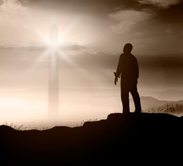 Praise and worship concept: Silhouette of man on top of mountain over blurred cross background