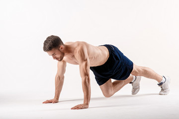 young man with a beard of a sports physique doing push-ups from the floor on a white isolated background, sportsman goes in for sports