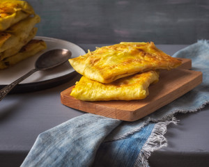 Hot baked sandwiches with meat and vegetables, serving on a wooden stick, in the background a stack of sandwiches on a plate