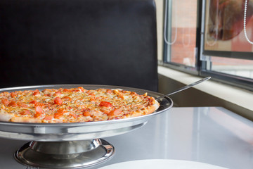 Pizza on iron tray on table in cafe. Close-up, copy space