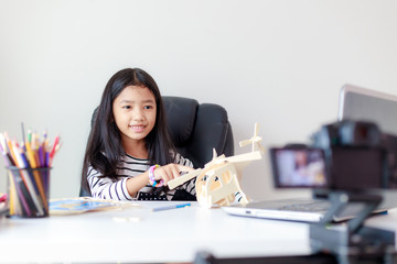 Happy little Asian girl sitting at the white table and live streaming for social media with happiness by camera select focus shallow depth of field