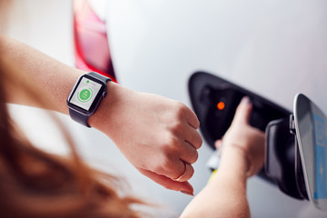 Man Charging Electric Vehicle With Cable Looking At App On Smart Watch