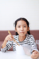 Happy little Asian girl sitting at white table to eating instant noodle  with deliciously select focus shallow depth of filed