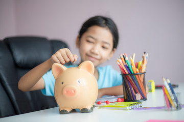Happy little asian girl putting money coin into piggy bank select focus shallow depth of field