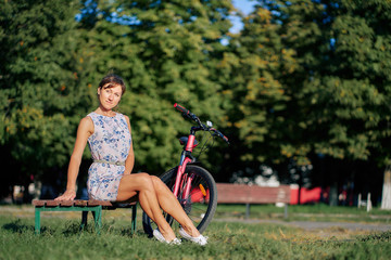 Fototapeta na wymiar young girl sitting on a park bench with a bicycle at sunset