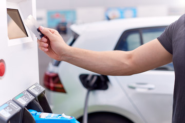 Man Charging Electric Vehicle Paying For Energy With Credit Card At Charging Station
