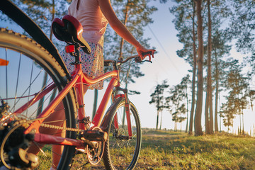 young woman with bike on autumn pine forest. sunset sun close-up