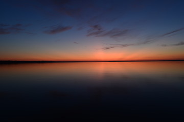 Fototapeta na wymiar Blue sky in a bright twilight glow in calmness on the horizon above water
