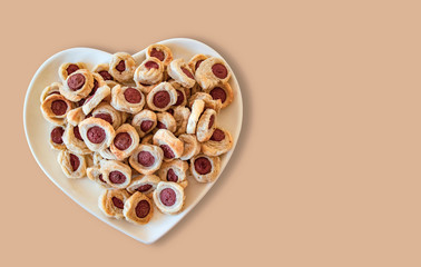 pastry and mini hot dogs in heart-shaped plate, on wood table background, fast food.