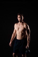Obraz premium Young bearded man with a kettlebell in his hands on a black background. bare-chested athlete