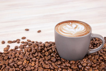 Latte coffee in dark coffee cup with coffee beans on isolated wood textured background