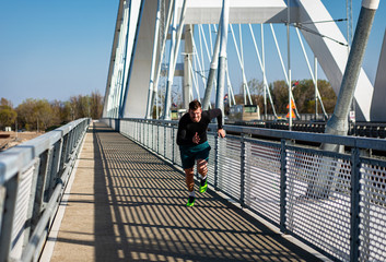 Young male runner sprinting on the bridge in the city during day.