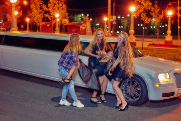 night portrait of a group of girls on a background of a white limousine. they are having fun. night...