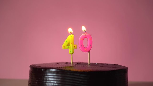 Chocolate birthday cake on pink background with yellow and pink number forty candle in middle electric lighter lighting candle