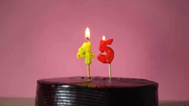 Chocolate birthday cake on pink background with yellow and red number forty five candle in middle electric lighter lighting candle