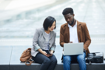 Portrait of two ethnic young people using laptop together outdoors while working on business project using wi-fi, copy space