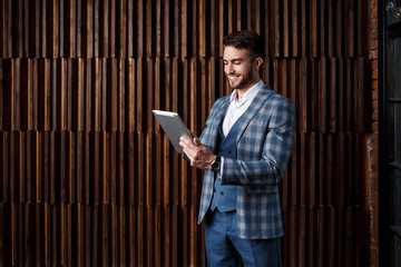 young successful businessman with a beard in a luxurious blue checked suit. Man works on a tablet in a loft office