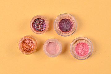 Cosmetics. Makeup. Jars with  crumbly bright shadows, glitter. Pink,peach, golden colors on beige background. Closeup. Space for text or design.