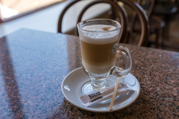 A tall glass of cappuccino on the table in the cafe.