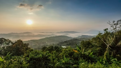 Mountain view panorama misty morning of top hills and green forest around with sea of fog with yellow sun light in the sky background, sunrise at ITTI View Point, Khao Kho, Phetchabun, Thailand.