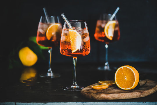 Aperol Spritz aperitif with oranges and ice in glass with eco-friendly glass straw on concrete table, black background, selective focus. Summer refreshing drink concept