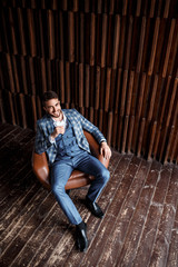 Young successful businessman in a blue suit in a cage is sitting in a leather chair. young man with a beard smiling and looks into the distance