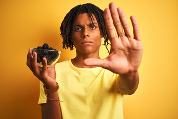 Afro american with dreadlocks holding blackberries over isolated yellow background with open hand...