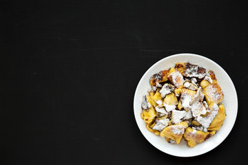 Homemade german Kaiserschmarrn pancake on a black surface, top view. Flat lay, overhead, from above. Copy space.