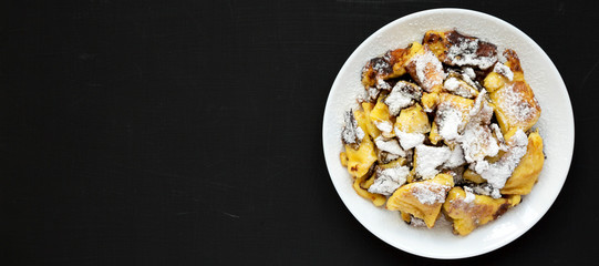 Homemade german Kaiserschmarrn pancake on a black surface, top view. Flat lay, overhead, from above. Space for text.