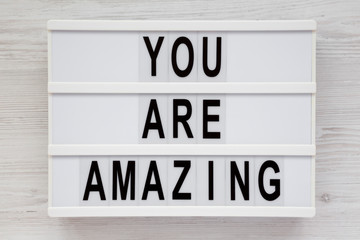 'You are amazing' words on a lightbox on a white wooden background, top view. Overhead, from above. Flat lay. Close-up.