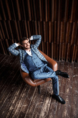 Young successful businessman in a blue suit in a cage is sitting in a leather chair. young man with a beard smiling.