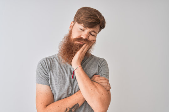Young redhead irish man wearing t-shirt standing over isolated grey background thinking looking tired and bored with depression problems with crossed arms.