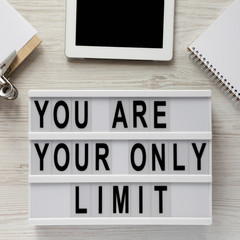 'You are your only limit' words on a modern board, clipboard with blank sheet of paper, tablet, notepad on a white wooden surface, top view. From above, overhead.