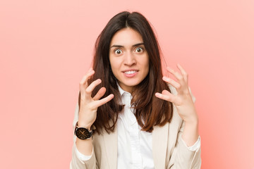 Young brunette business woman against a pink background upset screaming with tense hands.