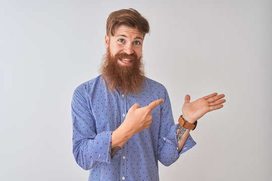 Young redhead irish man wearing casual shirt standing over isolated white background amazed and smiling to the camera while presenting with hand and pointing with finger.