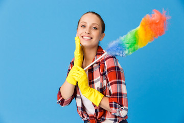 Portrait of optimistic housewife wearing yellow rubber gloves holding colorful duster while doing...