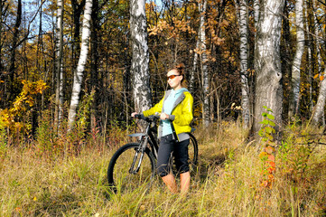 Fototapeta na wymiar Young slim girl on a bicycle in autumn birch forest