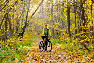 Girl on bicycle on a path in the autumn forest