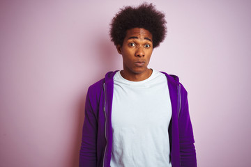 Young african american man wearing purple sweatshirt standing over isolated pink background skeptic...