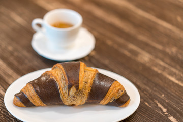 Fresh and tasty croissants with chocolate and cup of coffee on wooden background. copy space