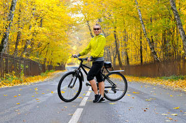 Girl with a bicycle on the road among autumn forest