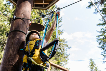 Small boy attaching carabiner to zip line on canopy tour in forest.