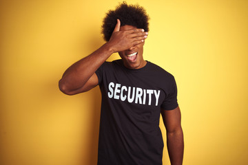 American safeguard man with afro hair wearing security uniform over isolated yellow background...