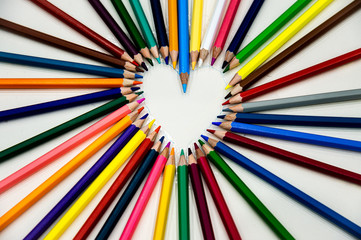 Top view sets of many different colored pencils display in heart shape on white background.
