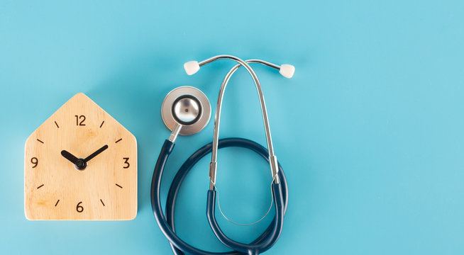 Wooden clock with stethoscope on blue background.