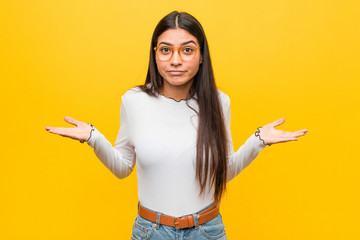 Young pretty arab woman against a yellow background doubting and shrugging shoulders in questioning gesture.
