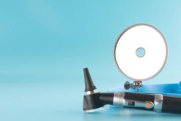 Otoscope with reflector mirror on blue background in health care concept.