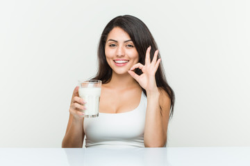 Obraz na płótnie Canvas Young hispanic woman holding a glass of milk cheerful and confident showing ok gesture.